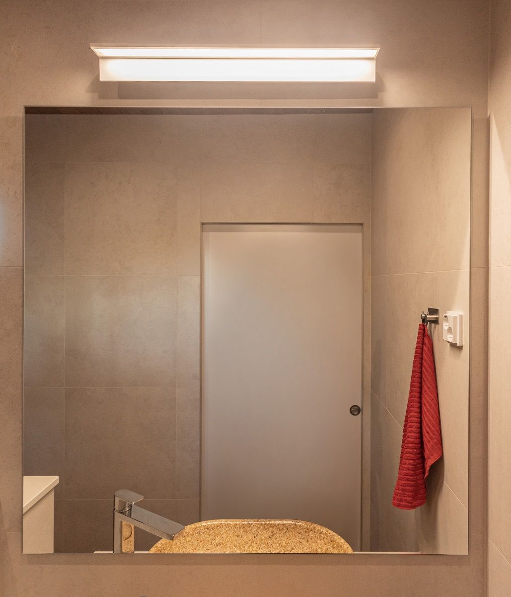 Nella zona doccia, sopra il lavabo, una lampada da parete BLADE600 bianca con cerchi in alluminio fornisce un'illuminazione uniforme. La luce ha una temperatura di colore calda di 3 000 Kelvin.